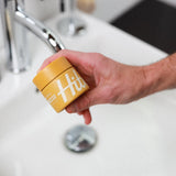 Yellow jar of Hitch Weightless Clay pomade being held in a man's hand.