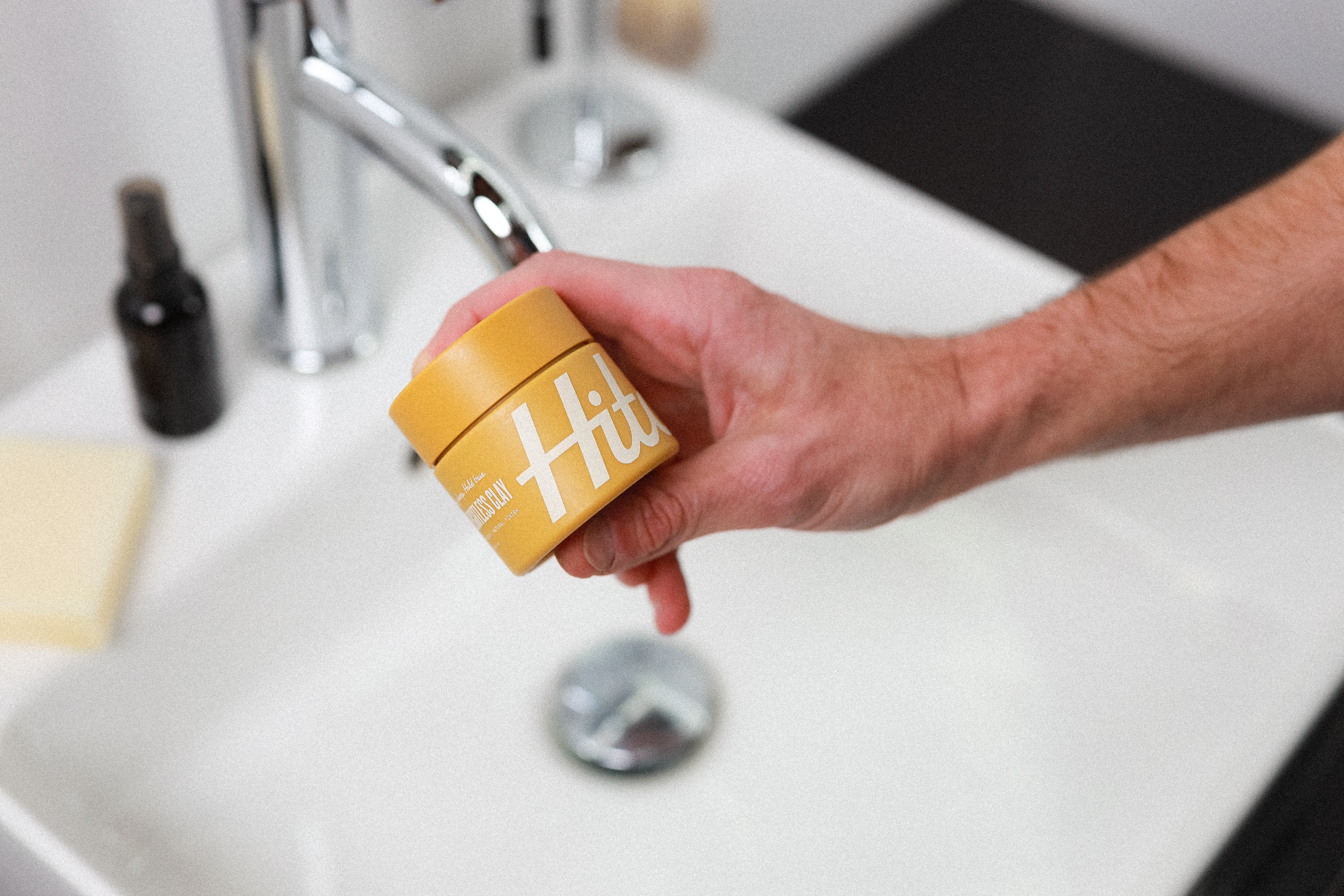 Yellow jar of Hitch Weightless Clay pomade being held in a man's hand.