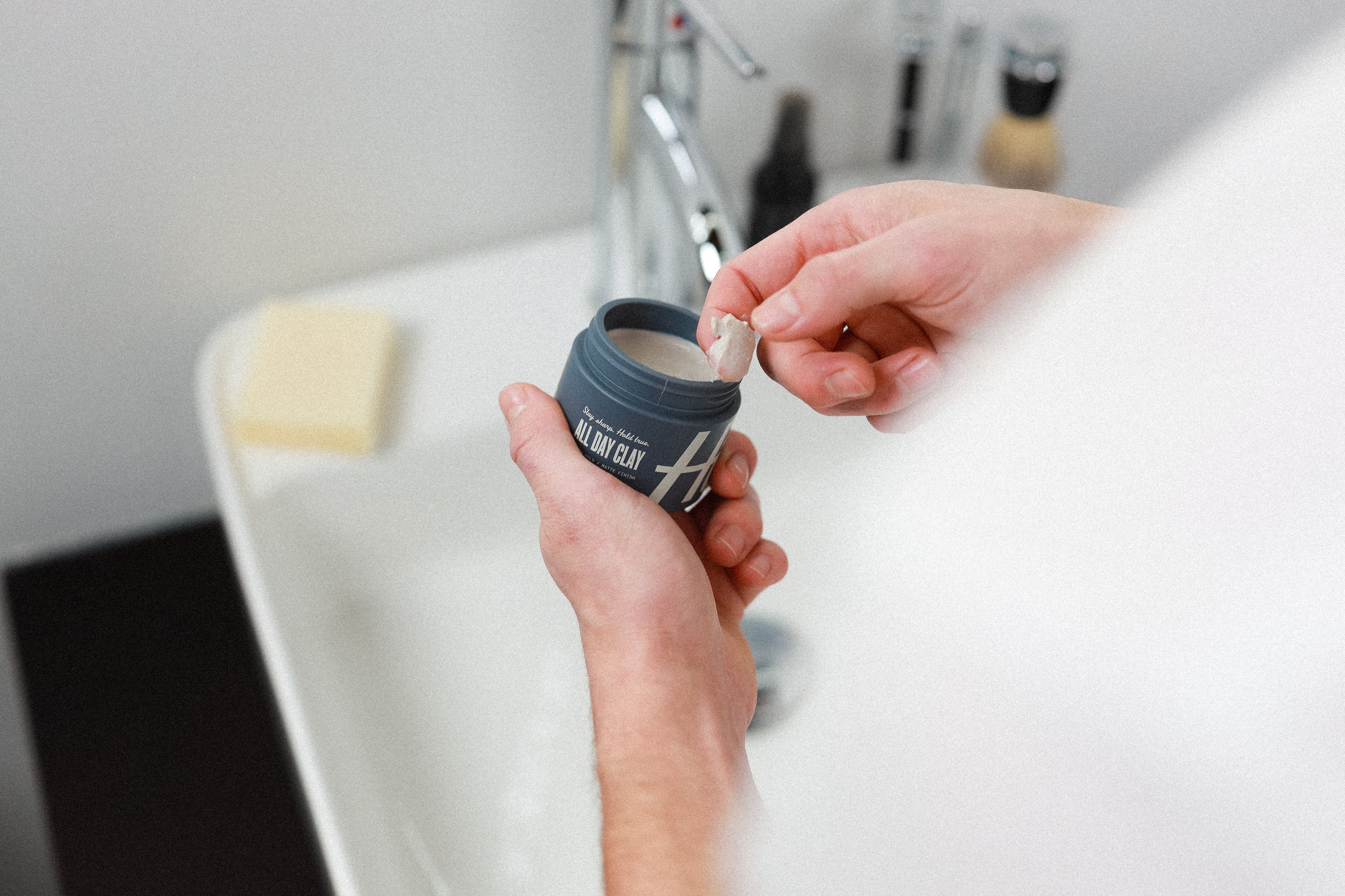 Man scooping hair clay out of blue "All Day Clay" jar.