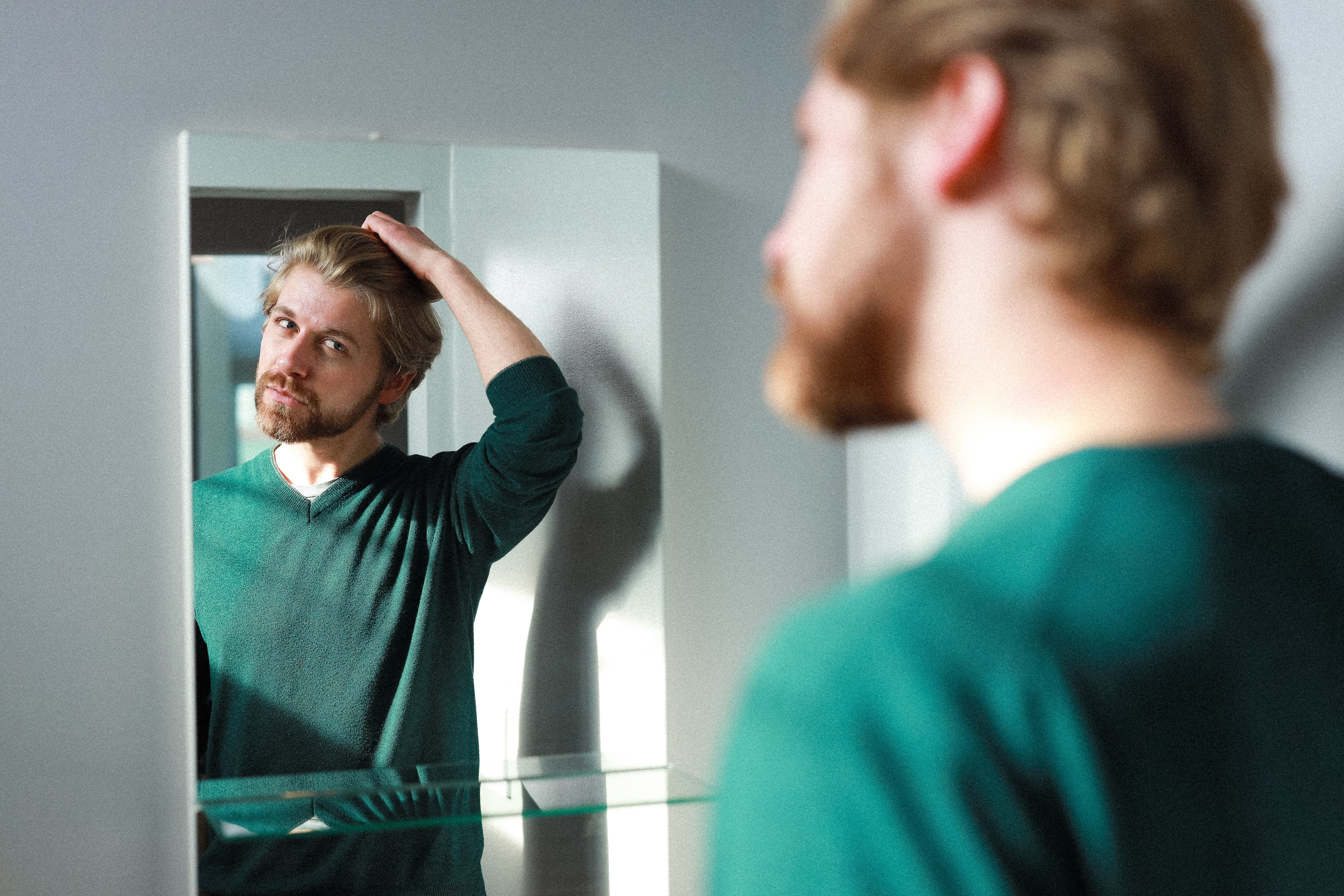 Young man styling his long hair in front of mirror.