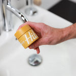 Yellow jar of Hitch product, "Weightless Clay" being held in a man's hand.