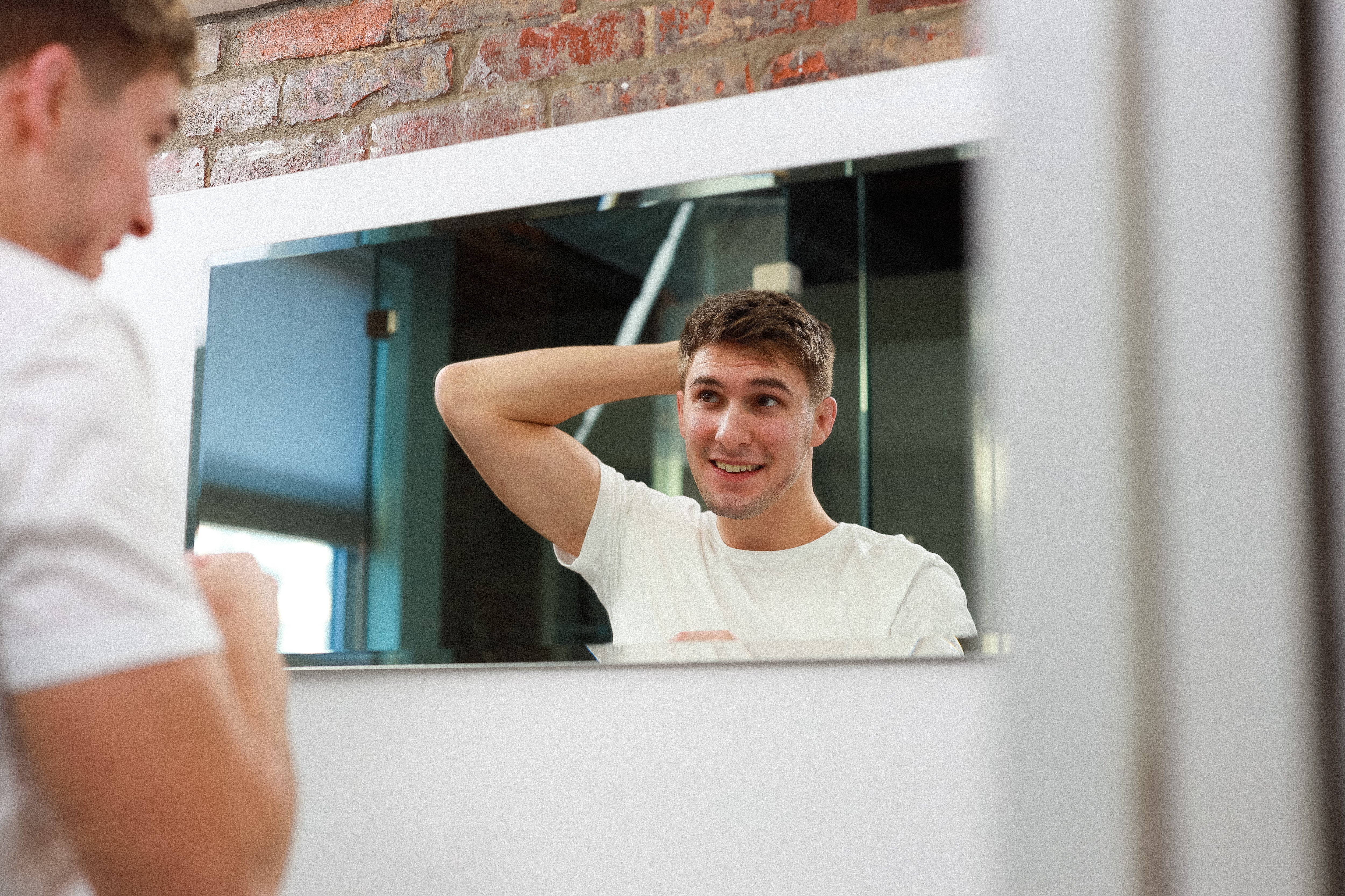 Young man styling his short hair in front of mirror.
