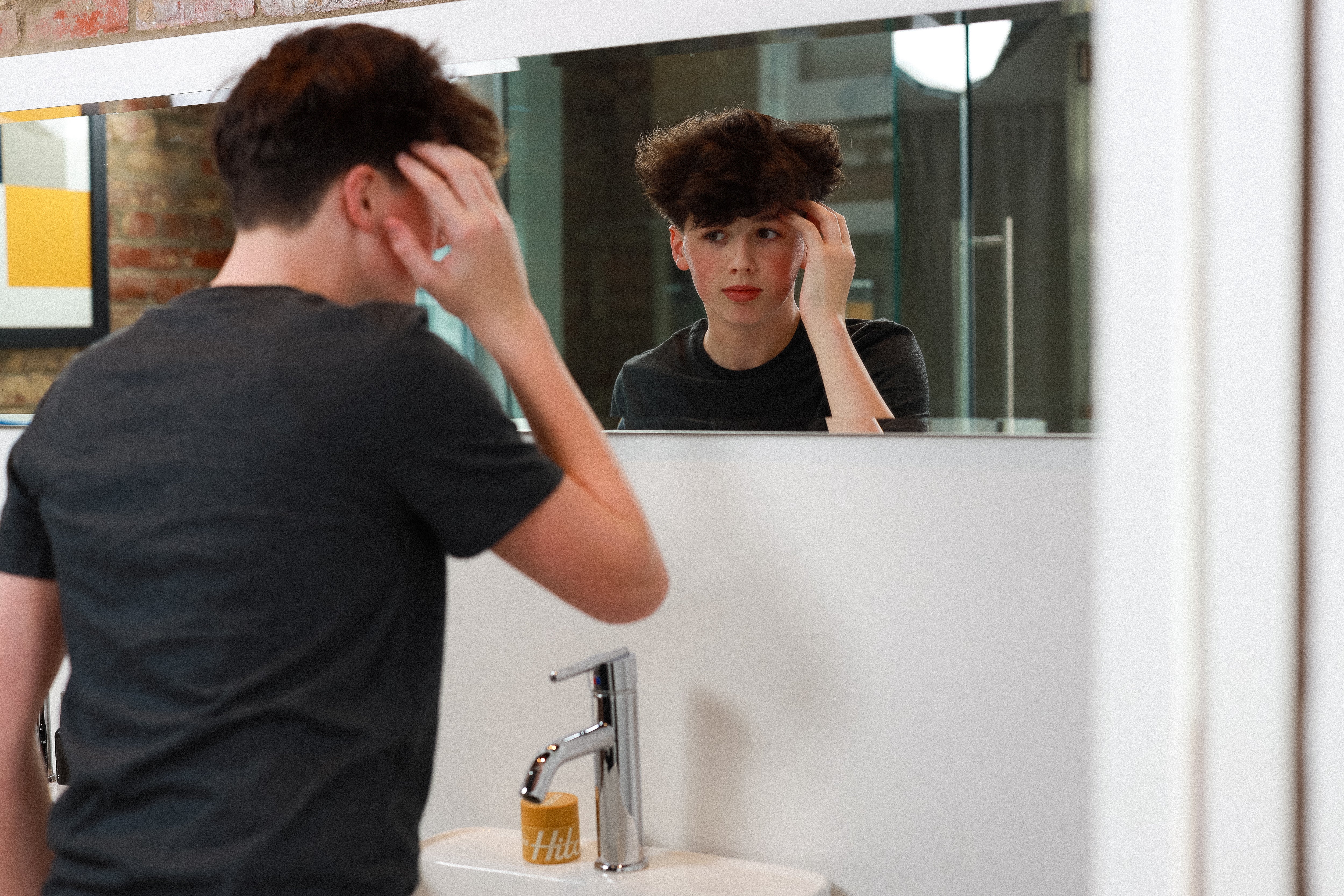 Young boy styling his medium length hair in front of mirror.