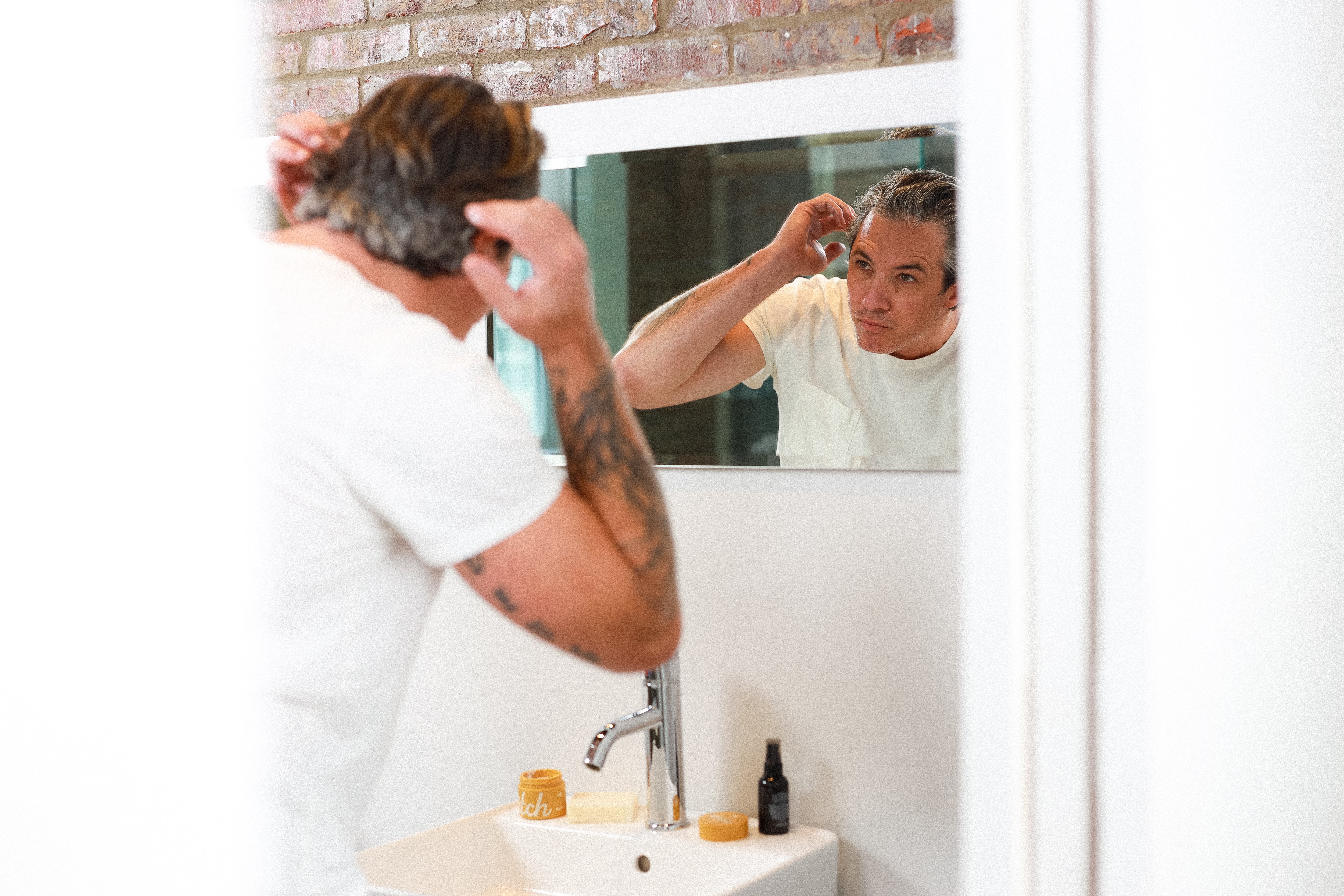 Man styling his hair while looking in mirror.